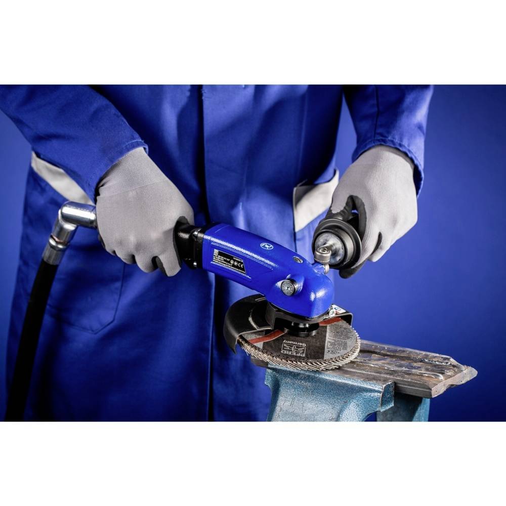 Eine Person in blauer Arbeitskleidung schleift Metall mit einem Elektrowerkzeug. Sie trägt Sicherheitshandschuhe.