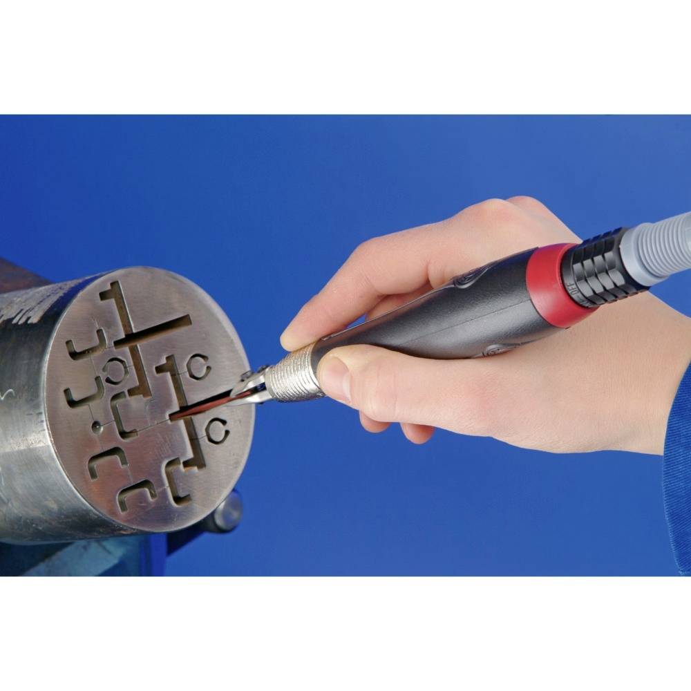 Eine Hand hält ein Gravurwerkzeug und bearbeitet ein metallisches Bauteil mit eingravierten Symbolen unter hellblauem Hintergrund.