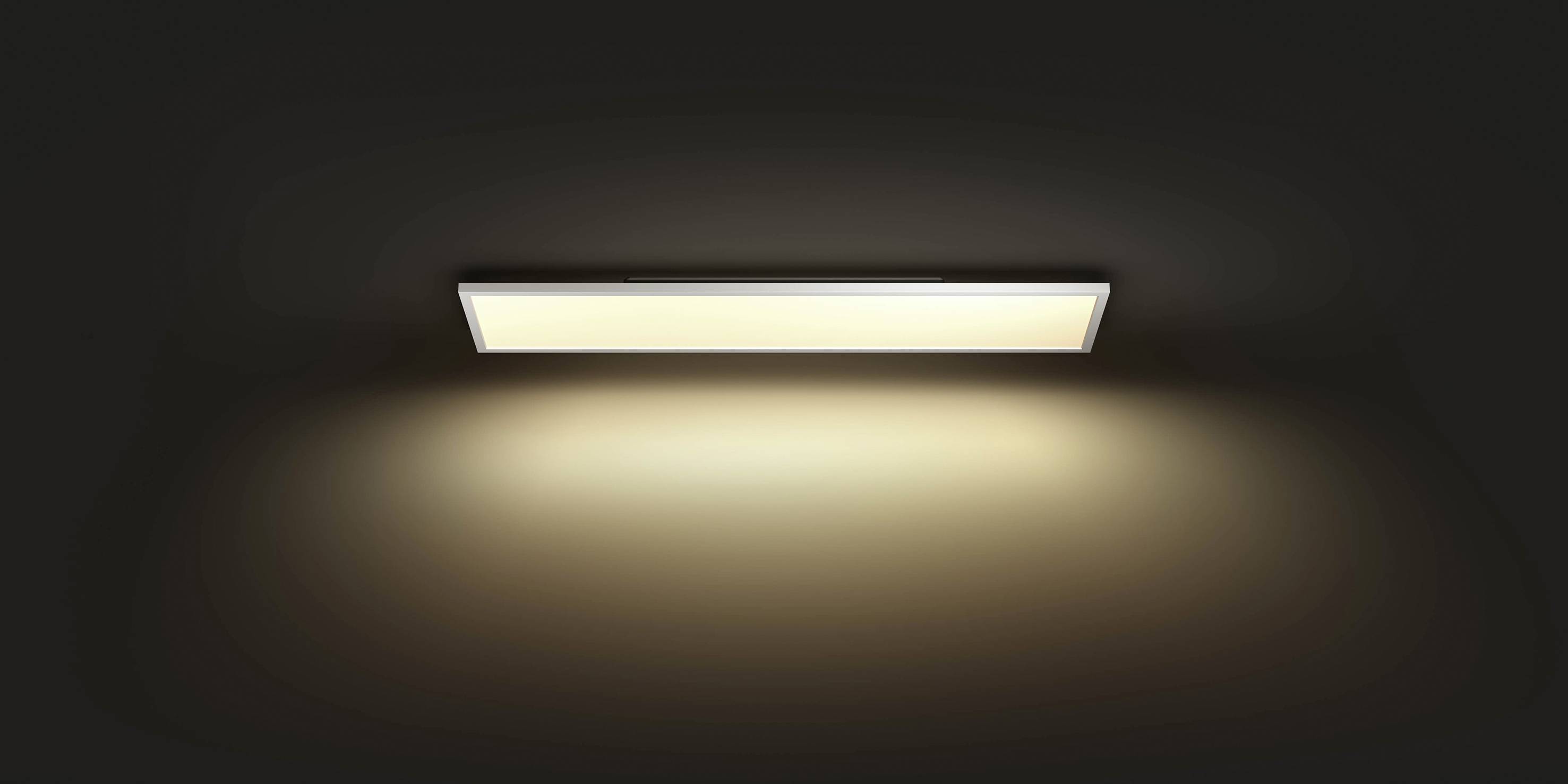 Eine rechteckige Deckenleuchte an einer dunklen Decke, die warmes, diffuses Licht ausstrahlt.