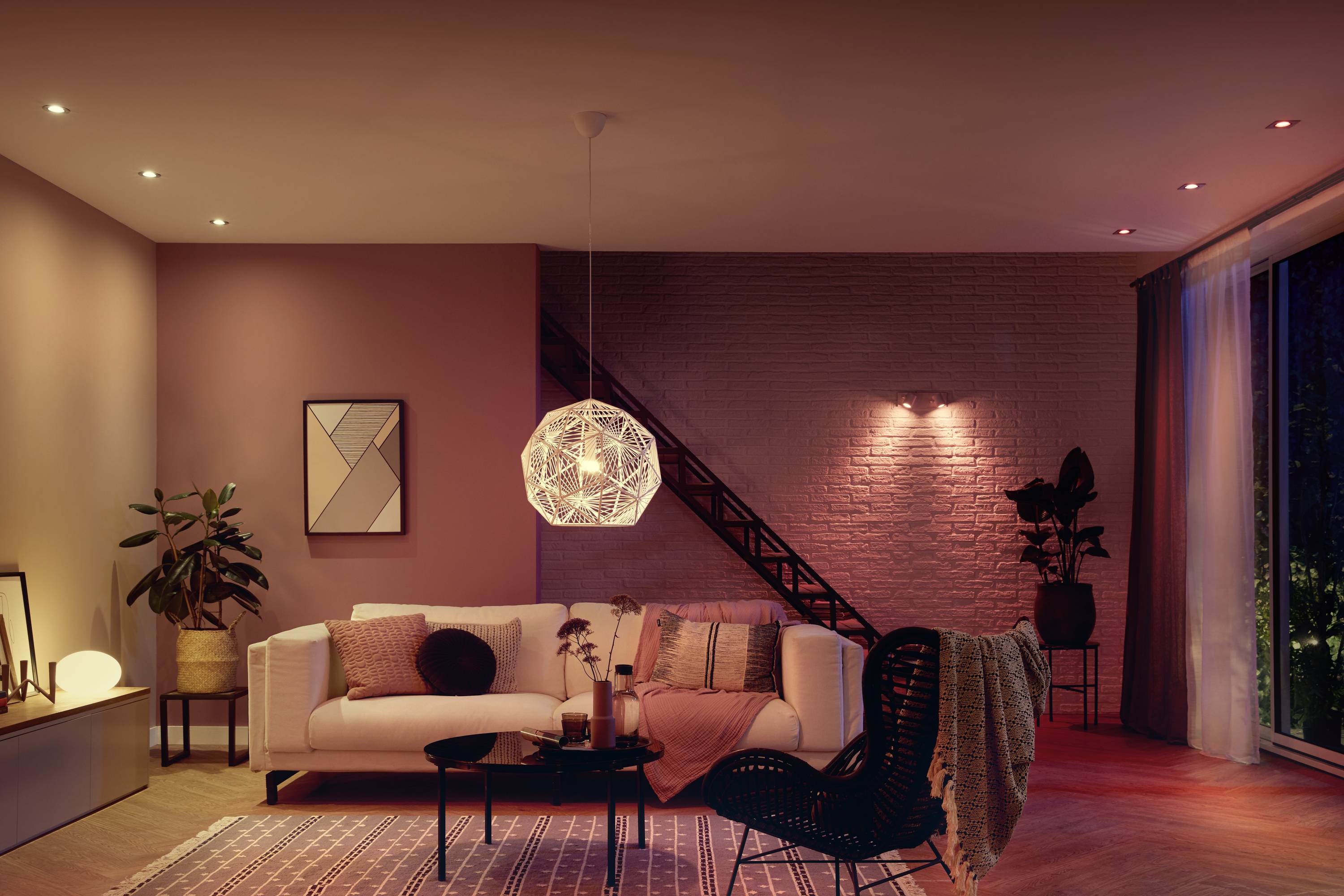 Ein stilvoll eingerichtetes Wohnzimmer mit einem weißen Sofa, modernen Möbeln und einer geometrischen Hängeleuchte in warmem Licht.