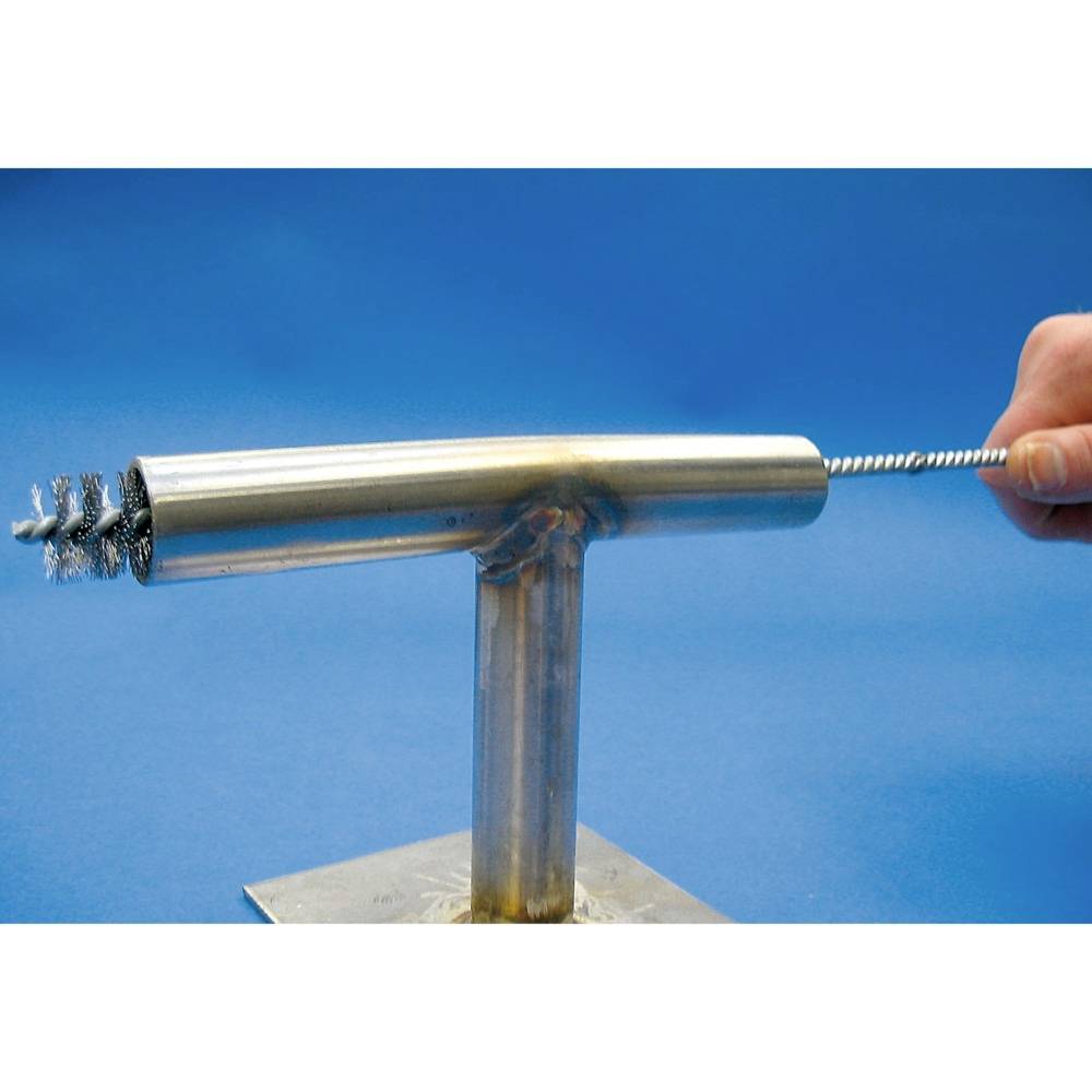 Eine Hand benutzt eine Drahtbürste, um ein T-förmiges Rohr aus glänzendem Metall zu reinigen. Der Hintergrund ist blau.
