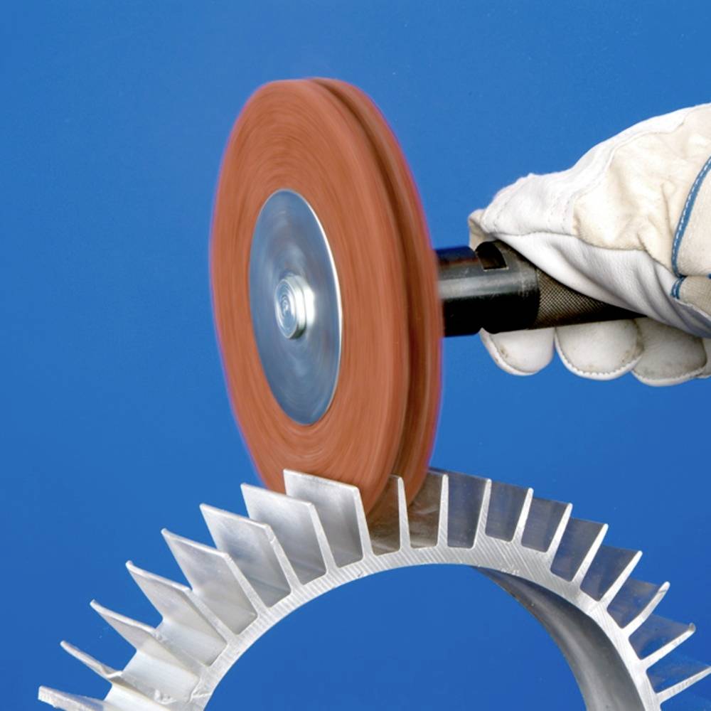 Eine Person in Schutzhandschuhen schleift ein metallisches Zahnraddetail mit einer rotierenden Schleifscheibe.