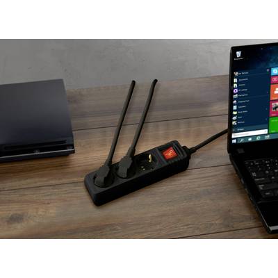 Laptop auf Holztisch, verbunden mit Mehrfachsteckdose. Zwei Stecker eingesteckt, einer frei. Links geschlossenes Gerät, möglicherweise weiteres Laptop.