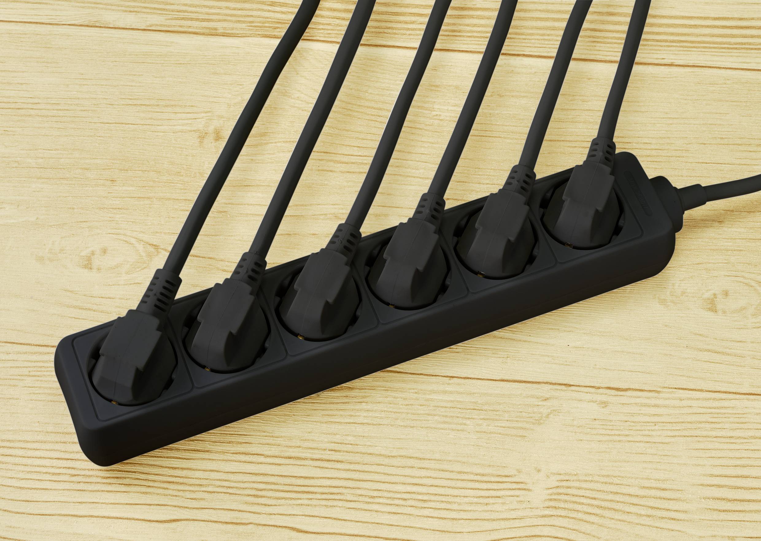 Sechs schwarze Stecker sind in eine schwarze Mehrfachsteckdose eingesteckt, die auf einem Holztisch liegt.