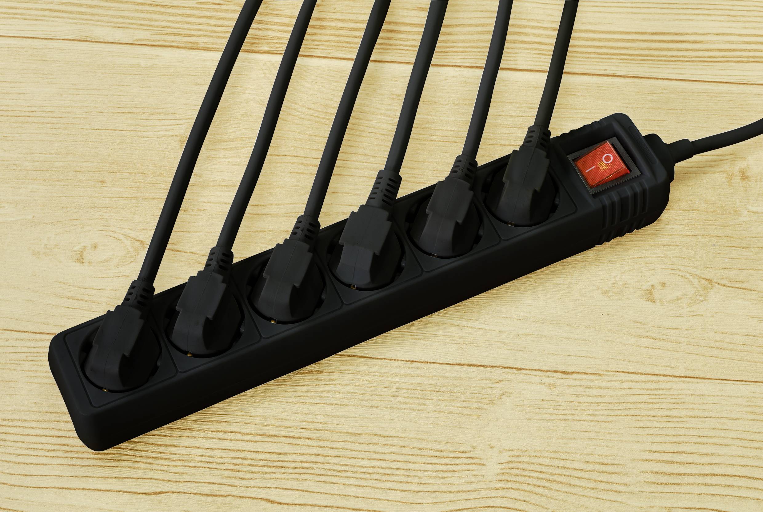 Ein schwarzer Mehrfachstecker mit sechs angeschlossenen Netzkabeln und einem roten Kippschalter auf einem Holztisch liegend.