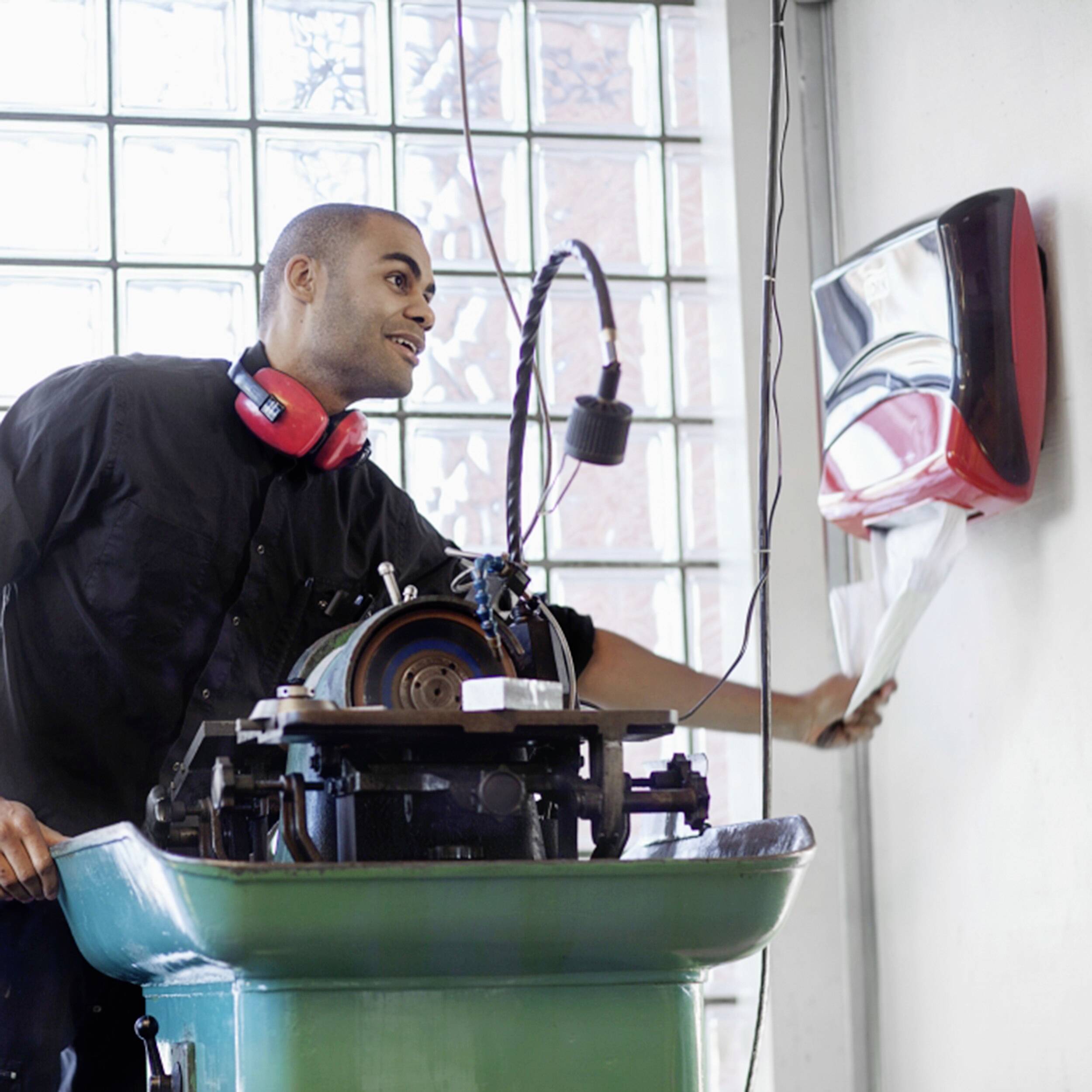 Ein Mann in Arbeitskleidung benutzt Papierhandtücher neben einer Nähmaschine in einer hellen Werkstatt.