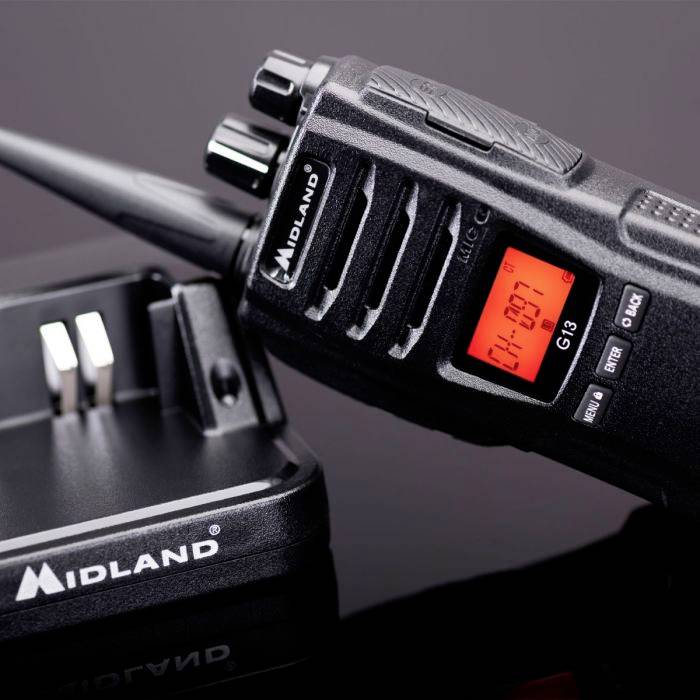 Ein schwarzes Walkie-Talkie mit rotem Display zeigt 'CH 07'; daneben eine Ladestation.
