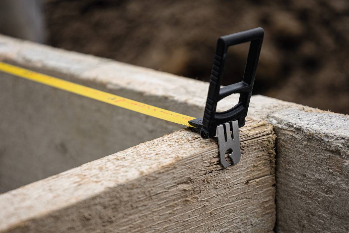 Ein Maßband misst die Länge eines Holzbretts auf einer Baustelle. Es zeigt etwa 97 Zentimeter an.