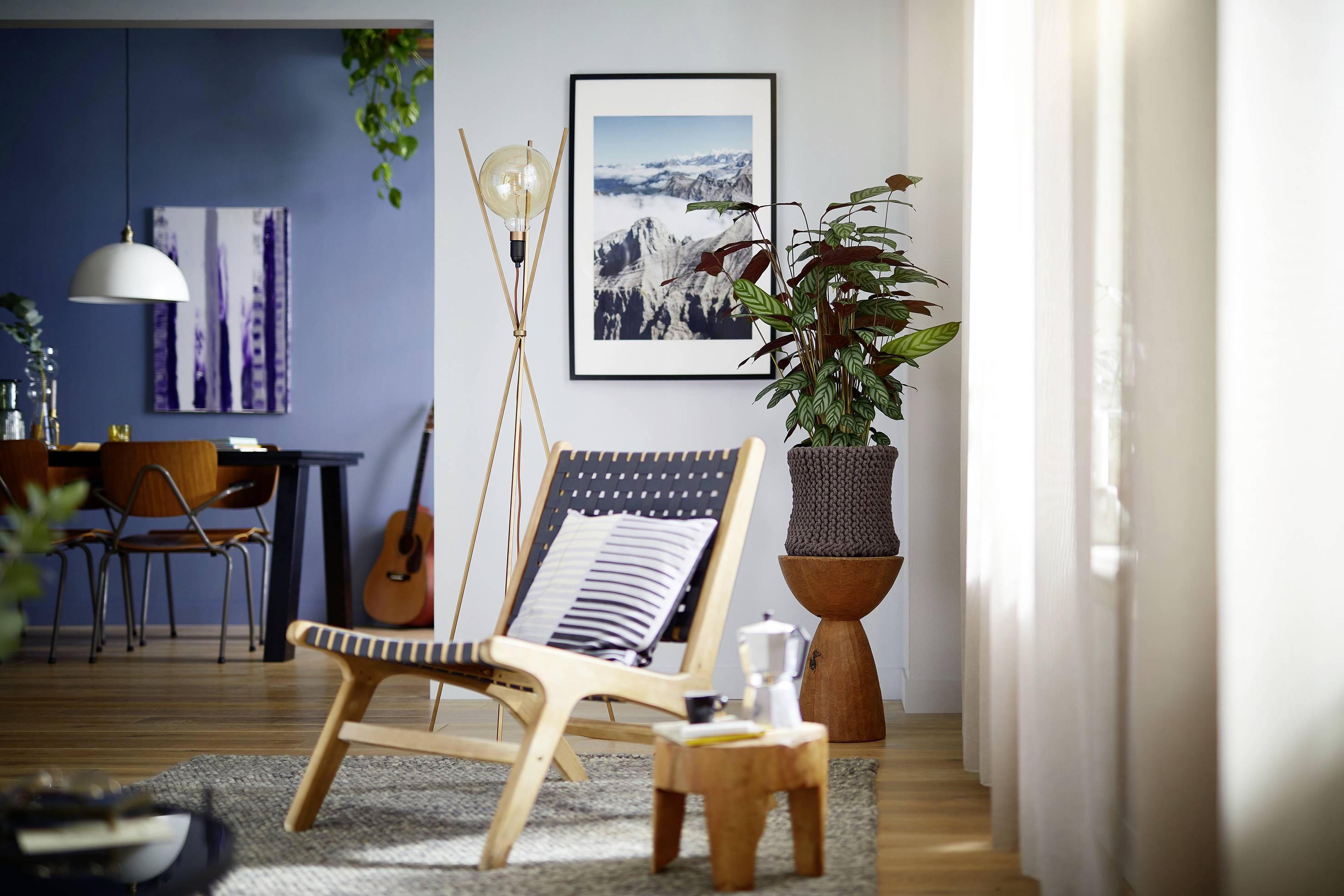 Gemütliches Wohnzimmer mit modernem Sessel, Pflanze und Kunst an den Wänden; im Hintergrund Essbereich mit Esstisch und Gitarre.