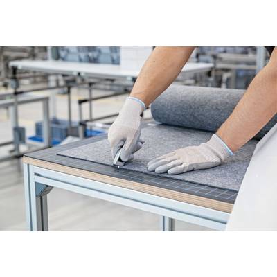 Eine Person mit Handschuhen schneidet mit einem Messer grauen Filz auf einem Tisch in einer Werkstatt.