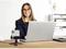 Eine Frau sitzt am Schreibtisch und arbeitet am Laptop. Vor ihr steht ein Smartphone auf einem Stativ. Im Hintergrund ist ein Regal.