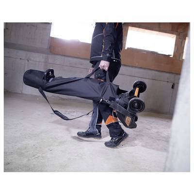 Eine Person trägt einen zusammengeklappten E-Scooter in einer schwarzen Transporttasche an ihren Griffen in einem unfertigen Betonraum.