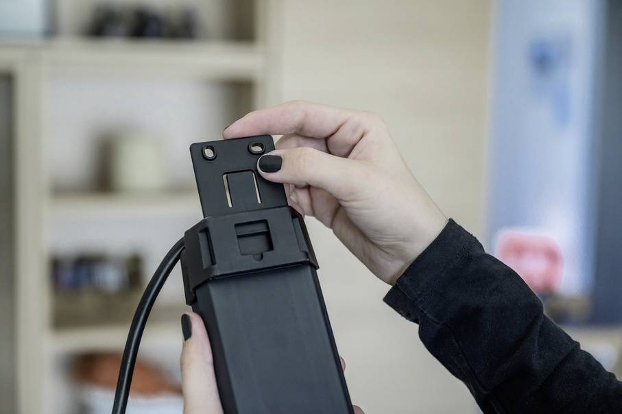 Person hält ein schwarzes, rechteckiges elektrisches Gerät mit Kabel. Es wird etwas zur Montage oder Demontage getan.