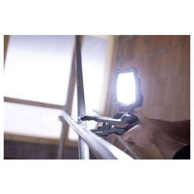 Person, die eine helle Arbeitsleuchte an einem Treppengeländer im Innenbereich befestigt, während sie in der Nähe eines Fensters arbeitet.
