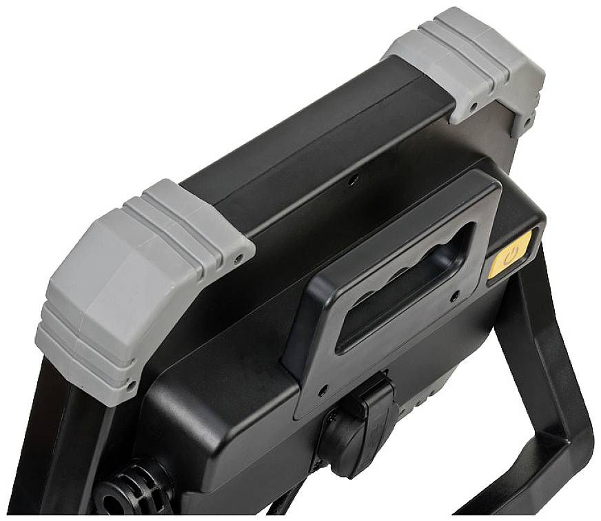 Tragbarer Baustrahler mit schwarzem Griff und grauen Schutzpolstern an den Ecken, geeignet zum einfachen Transport auf Baustellen.