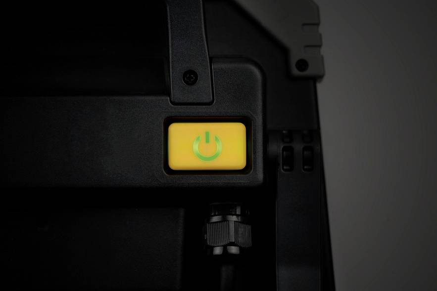 Ein gelber Ein-/Ausschalter an einem schwarzen Gerät, hervorgehoben und beleuchtet, deutet auf Betriebsbereitschaft hin.