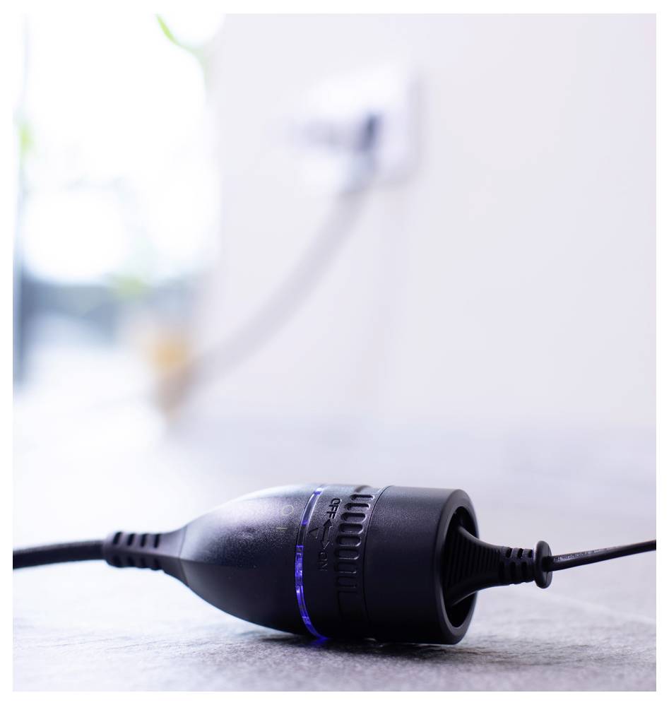 Schwarzer Elektrostecker oder Adapter liegt auf einem Boden, nicht angesteckt, mit Kabel, das sich nach rechts erstreckt.