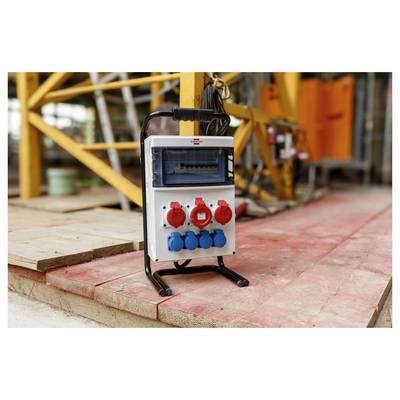 Tragbarer Stromverteiler mit roten und blauen Steckdosen und einem Display, der auf dem Boden einer Baustelle steht.