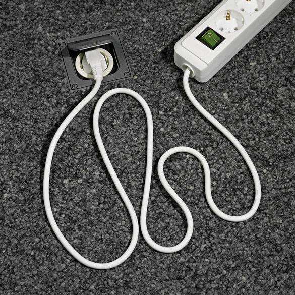 Eine weiße Steckdosenleiste mit Schalter und zwei Steckplätzen ist in eine graue Teppichfläche eingesteckt.