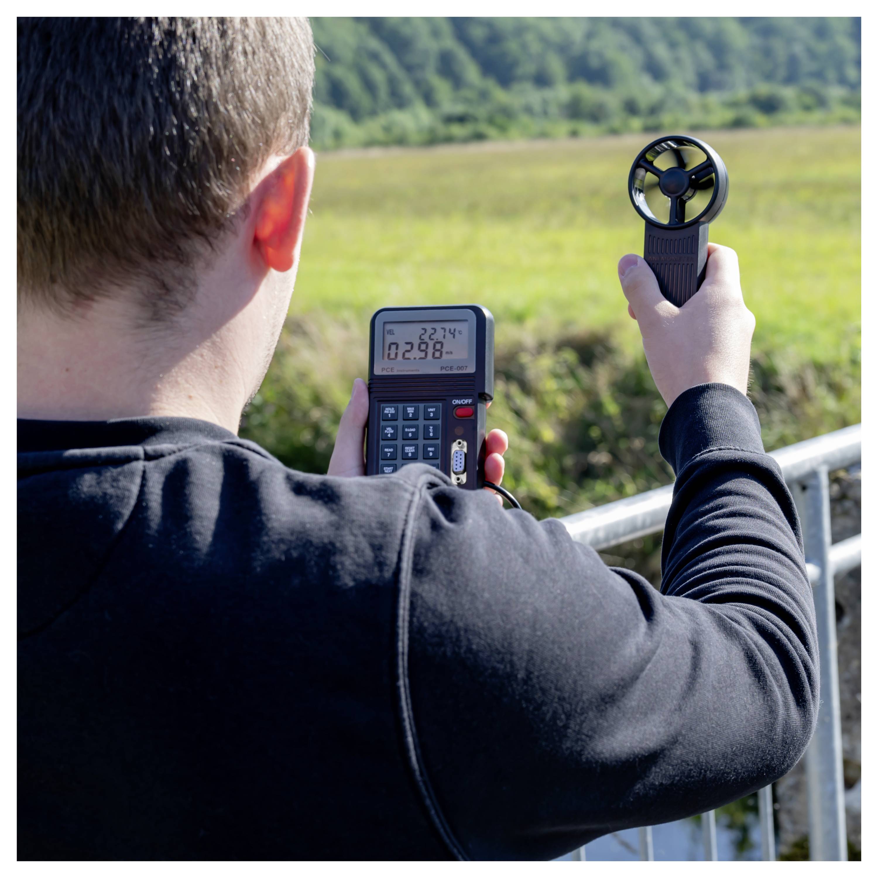 Eine Person, die die Windgeschwindigkeit auf einem Feld mit einem Anemometer und einem tragbaren Messinstrument misst.