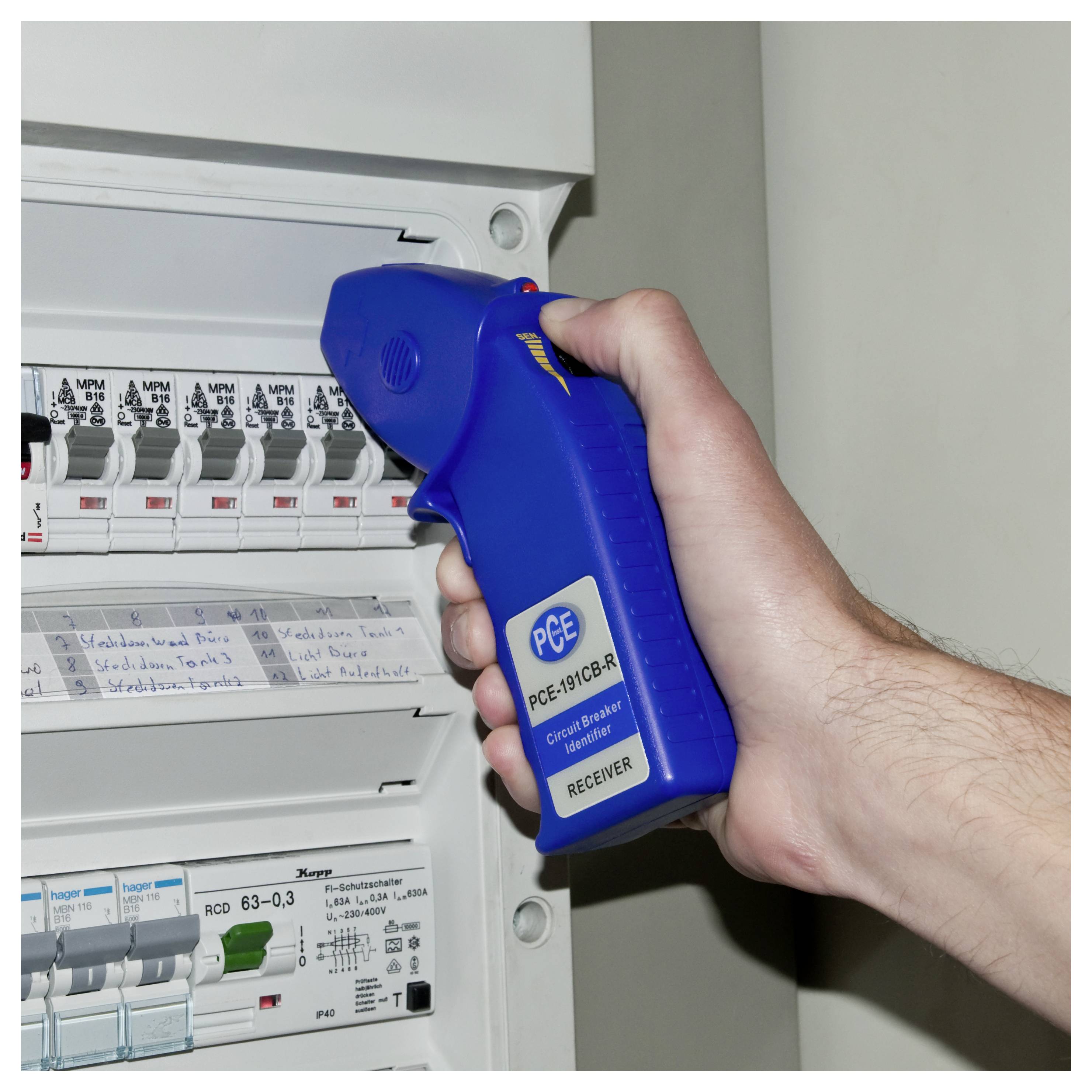 Hand mit einem blauen PCE-Empfänger zum Testen eines elektrischen Schutzschalters in einem offenen Sicherungskasten.