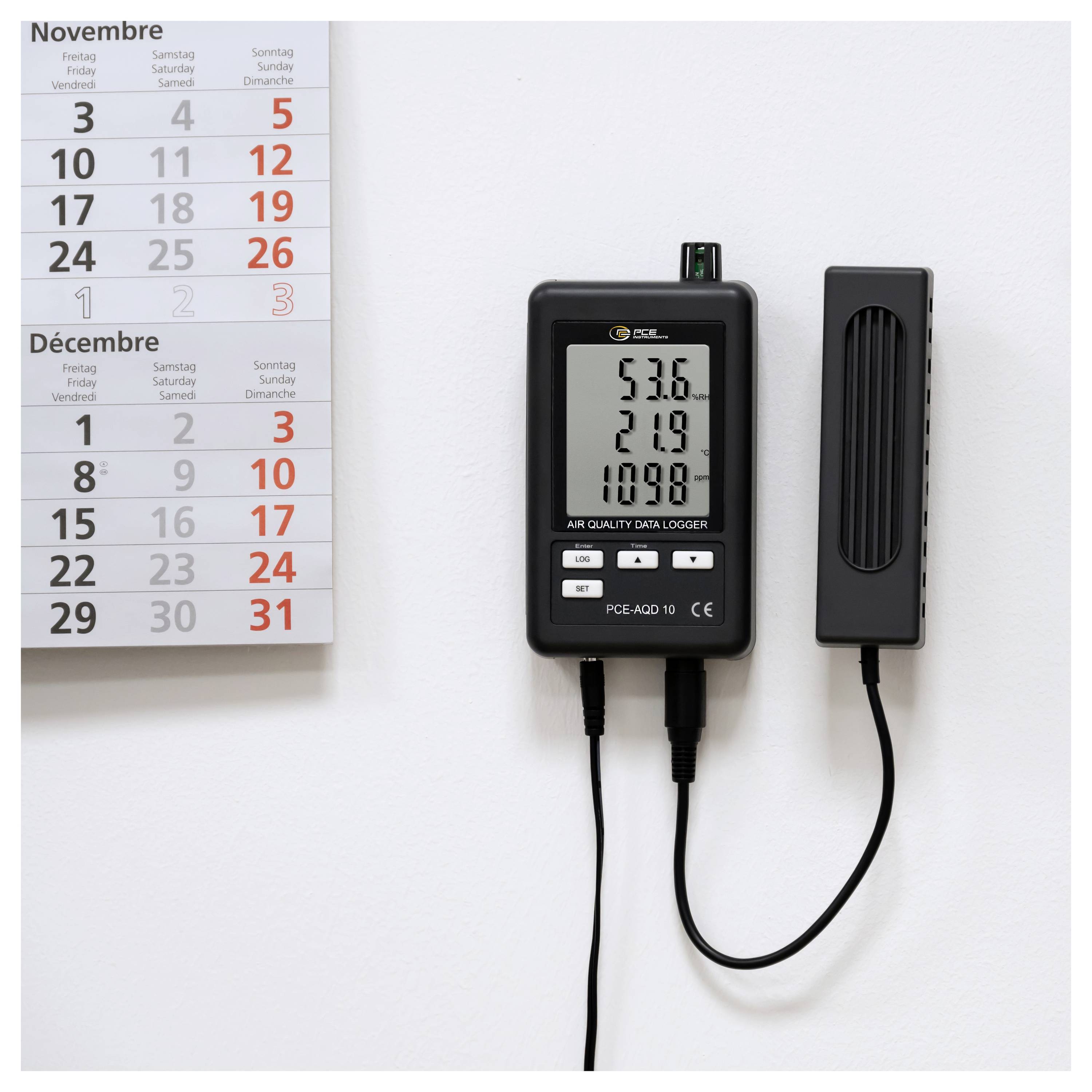 An der Wand montierter Datenlogger zur Luftqualitätsmessung zeigt die Werte 53,6, 21,9 und 109,8 neben einem Noveber-Dezember-Kalender an.