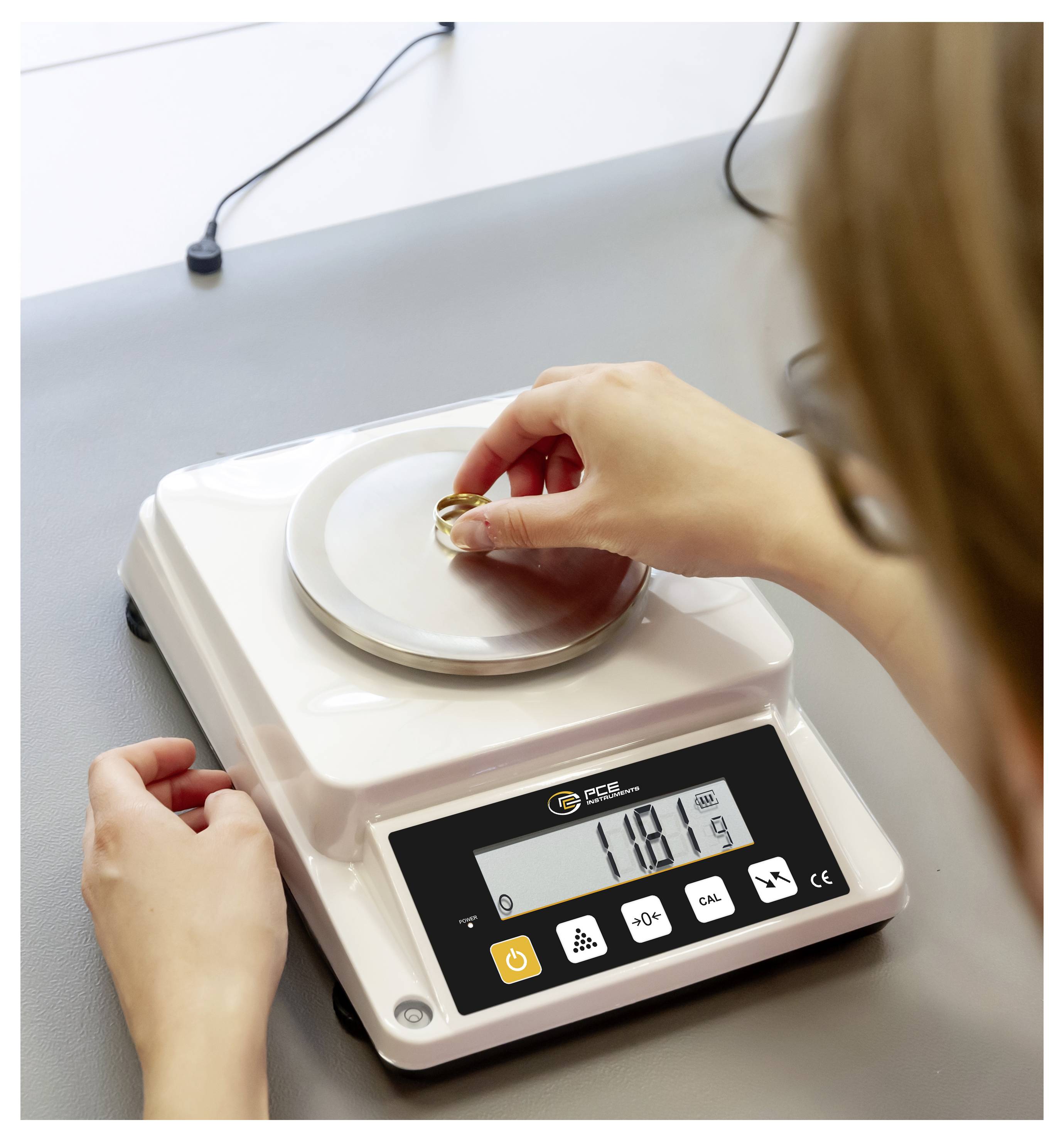 Person wiegt einen kleinen Ring auf einer digitalen Waage in einer Labor- oder Werkbankumgebung, wobei das Display 11,81 anzeigt.