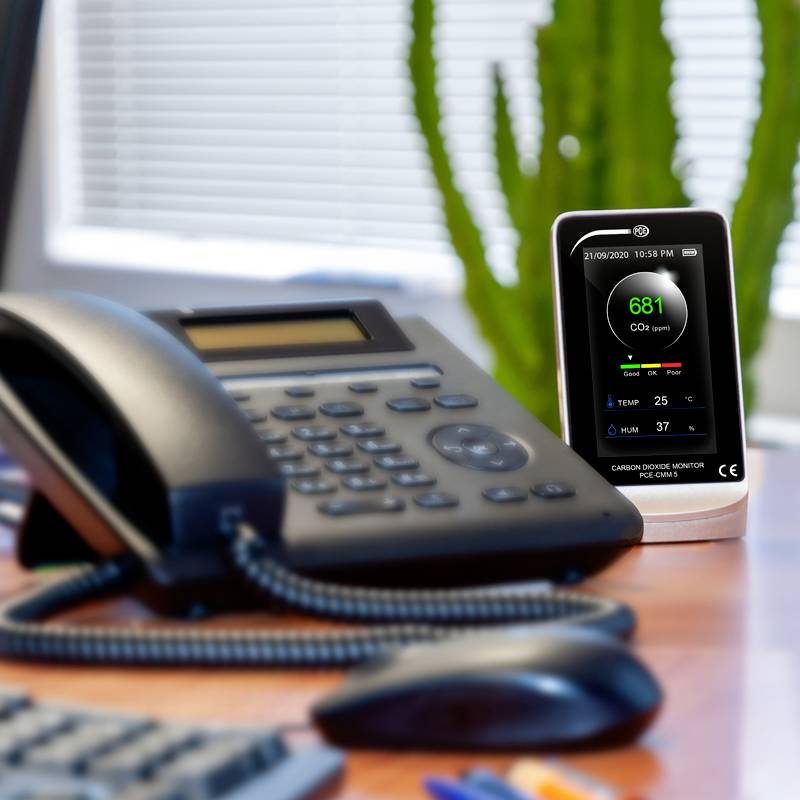 Ein Tisch mit einem Telefon und einem CO2-Monitor. Der Monitor zeigt '681 CO2 ppm' in Grün, was auf eine gute Luftqualität hinweist.