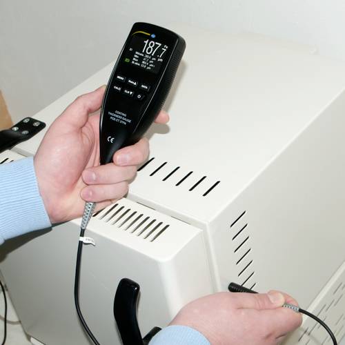Eine Person hält ein Gerät zur Temperaturmessung neben einem Heizkörper. Das Display zeigt 18,7 Grad und andere Messdaten an.