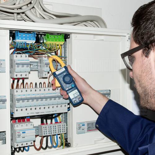 Ein Elektriker überprüft mit einem Strommessgerät die Sicherungen in einem Schaltschrank, um die elektrische Funktionalität zu gewährleisten.
