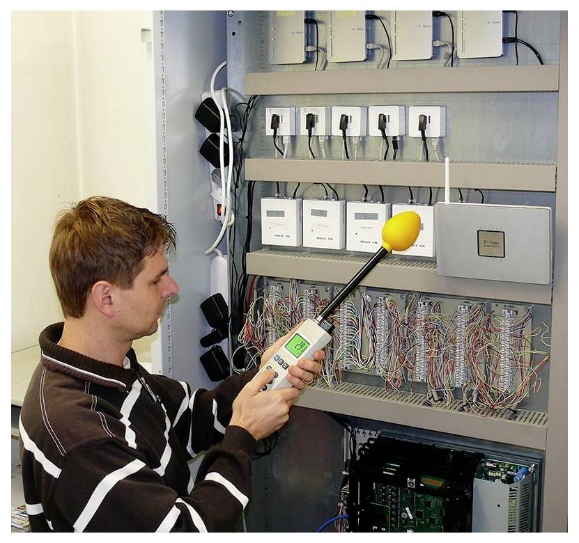 Techniker testet ein Bedienfeld mit einer tragbaren Sonde in einem Verdrahtungsschrank, der mit Modulen und Kabeln gefüllt ist.