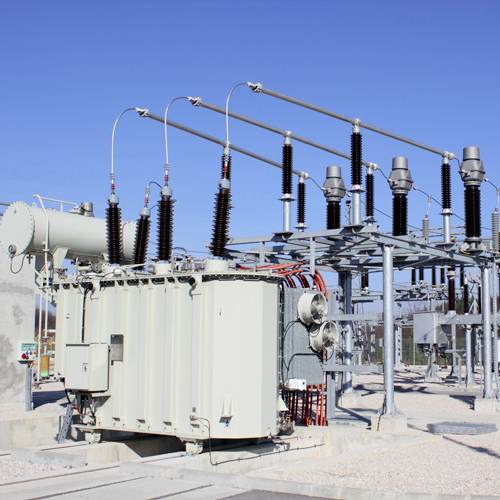 Ein Transformator in einem Umspannwerk bei klarem Himmel. Elektrische Leitungen und Isolatoren sind sichtbar.