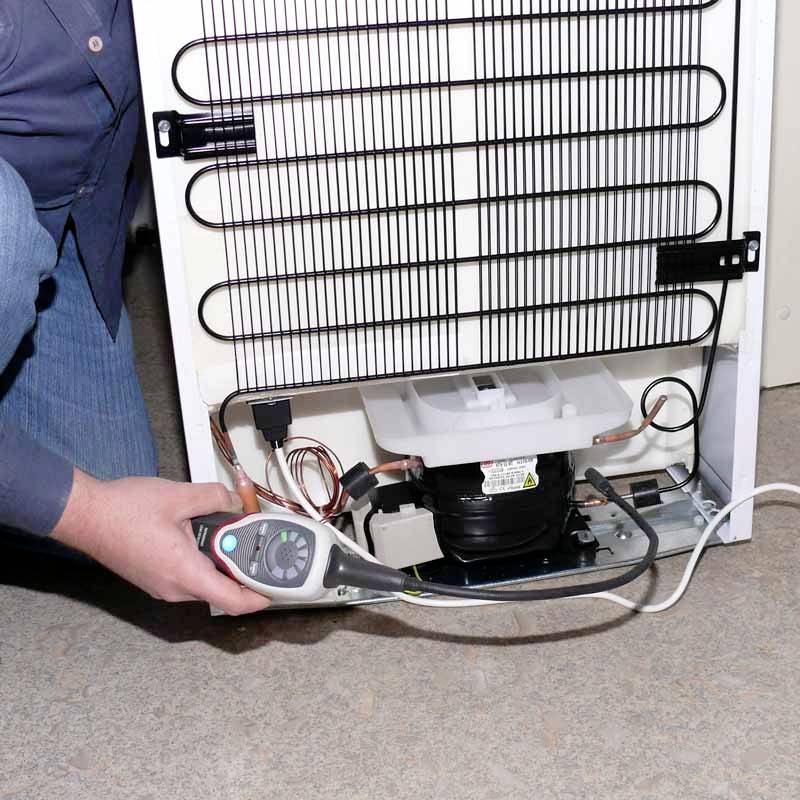 Eine Person führt eine Wartung an einem Kühlschrank durch. Sie hält ein Messgerät an der Rückseite des Geräts, um es zu überprüfen.
