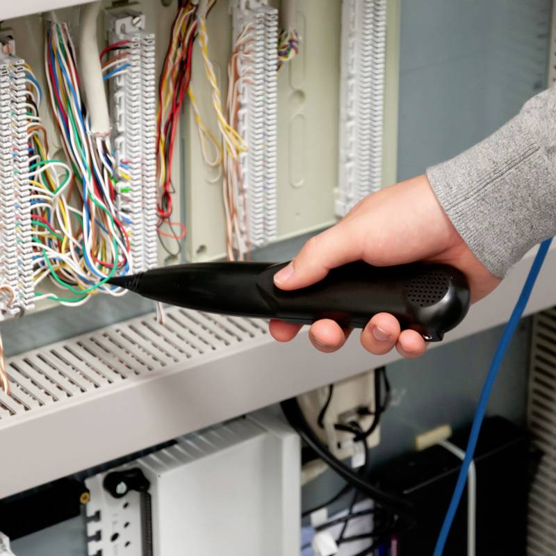 Eine Hand hält ein Prüfgerät an Netzwerkkabeln in einem Serverraum. Das Gerät testet die Verbindung der Kabel.