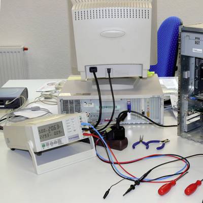 In einem Labor befindet sich auf einem Tisch ein offener Computer mit angeschlossenen elektronischen Messgeräten und Werkzeugen.