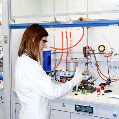 Eine Wissenschaftlerin arbeitet in einem Labor. Sie trägt einen weißen Laborkittel und führt ein Experiment mit chemischen Substanzen durch.