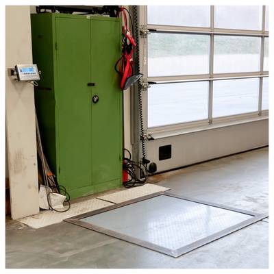 Industrielle Garage mit großem grünem Schrank, wandmontierter Schalttafel, hängenden Werkzeugen und einer Bodenluke in der Nähe des Garagentors.