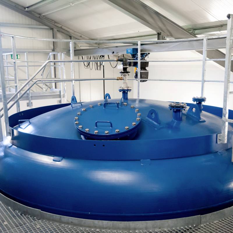 Ein großer blauer Tank mit mehreren Befestigungsstellen und Treppen, in einem industriellen Gebäude mit Metallstrukturen montiert.
