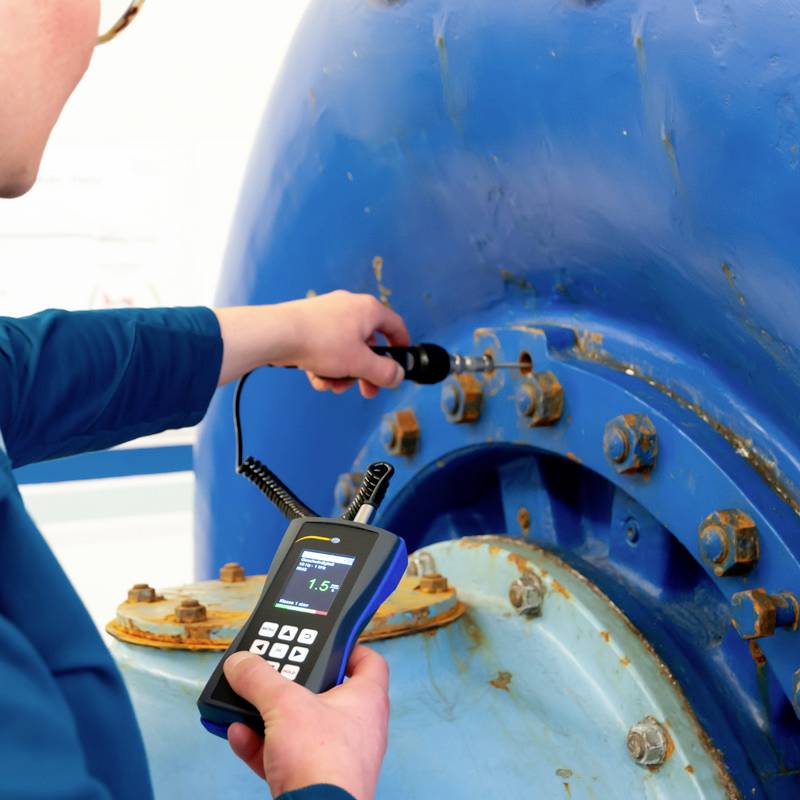 Eine Person misst die Dicke eines blauen Metallrohrs mit einem digitalen Messgerät.