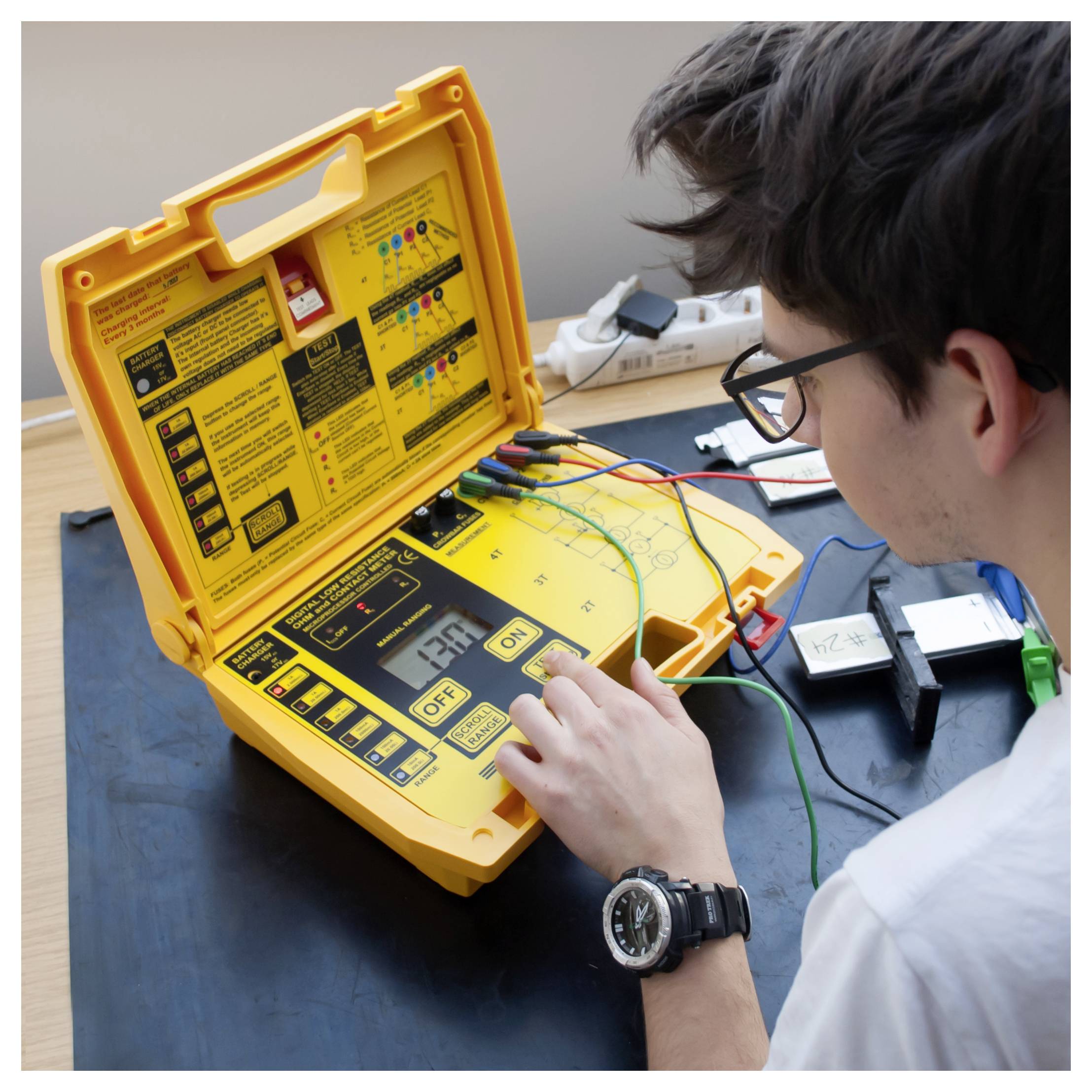 Techniker verwendet ein tragbares Elektrotestgerät auf einer Werkbank, mit Kabeln, die mit dem Gerät verbunden sind, und eine Person, die das digitale Display untersucht.