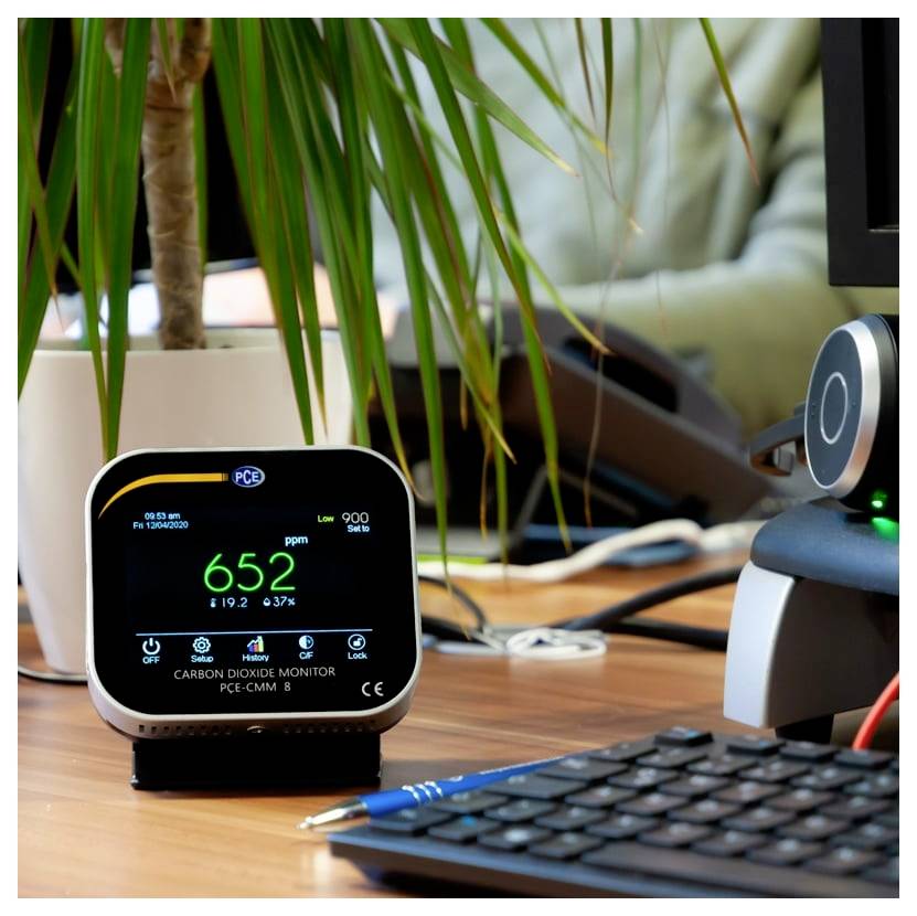 Digitales CO2-Messgerät auf einem Schreibtisch zeigt 652 ppm an, mit einer Tastatur, einem Stift, einer Pflanze und Büroausrüstung im Hintergrund.