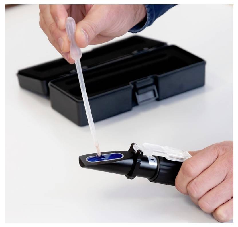 Eine Person nutzt eine Pipette, um Flüssigkeit in ein tragbares Bluttestgerät zu geben, das neben einer offenen Transporttasche steht.