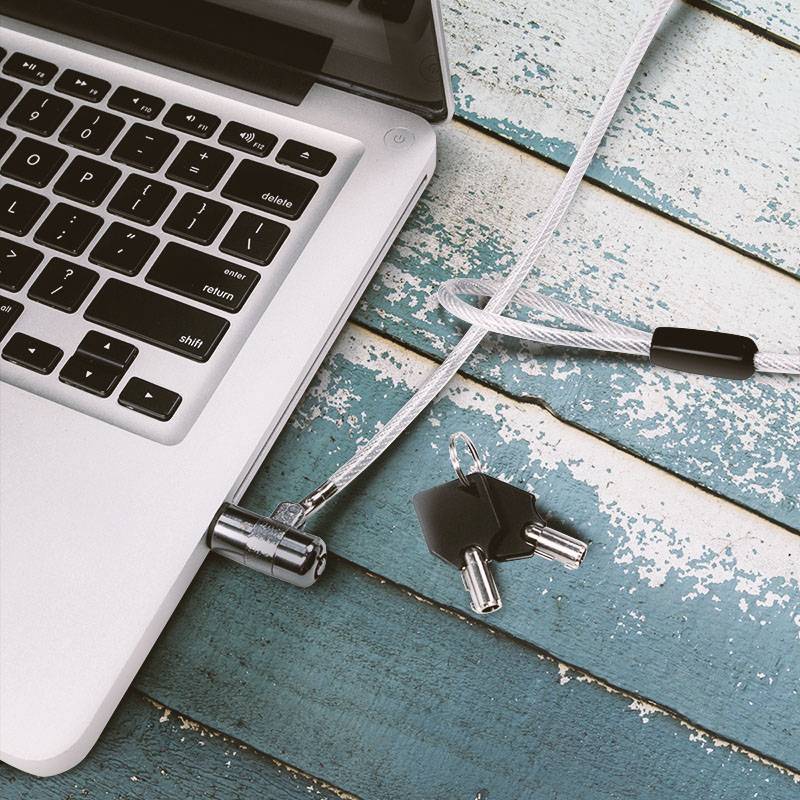 'Laptop mit angeschlossenem Diebstahlschutzkabel auf einem blauen, hölzernen Tisch. Zwei Schlüssel liegen daneben.'