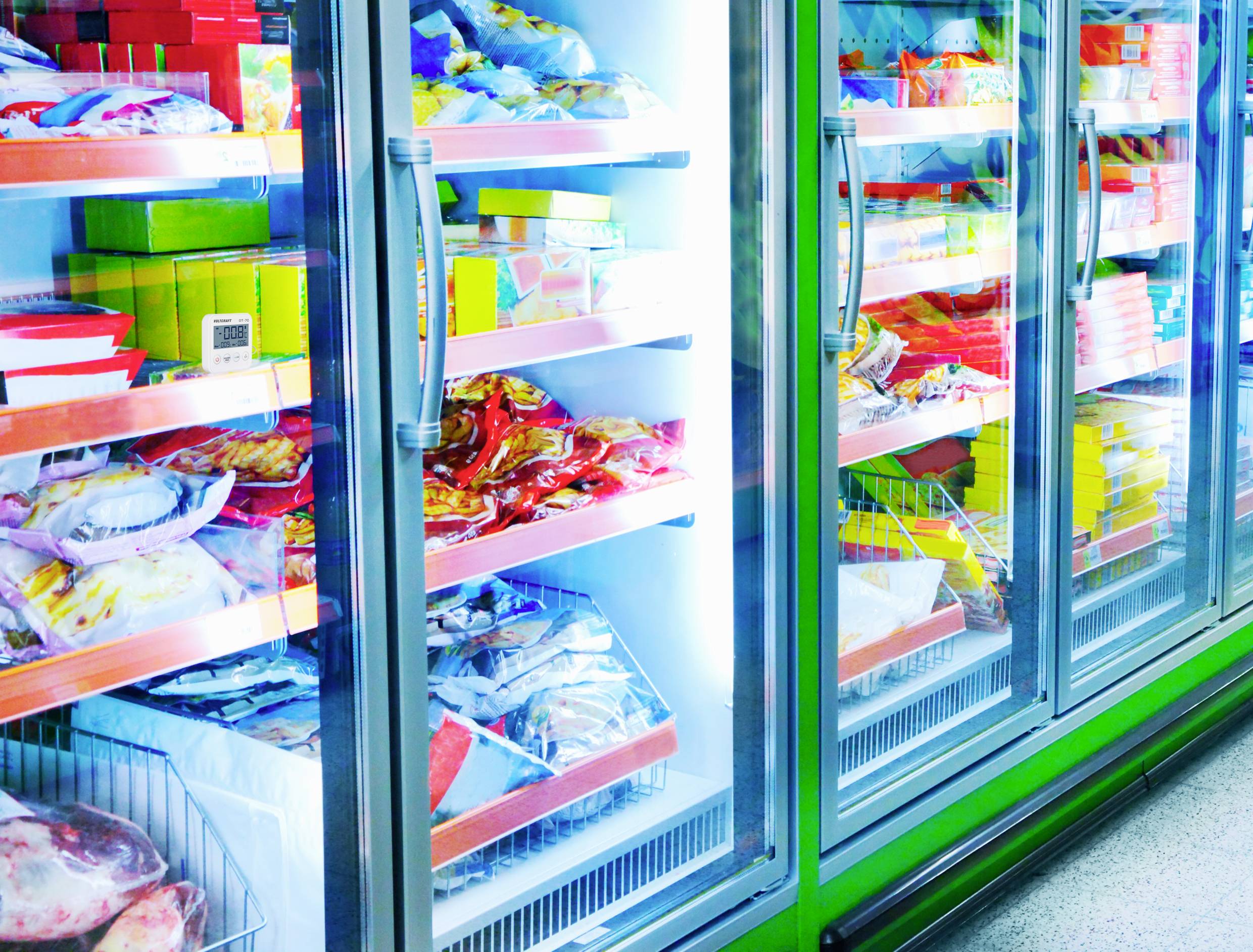 Kühlregal mit verschiedenen gefrorenen Lebensmitteln wie Pizza, Gemüse und Fleisch in einem Supermarkt.