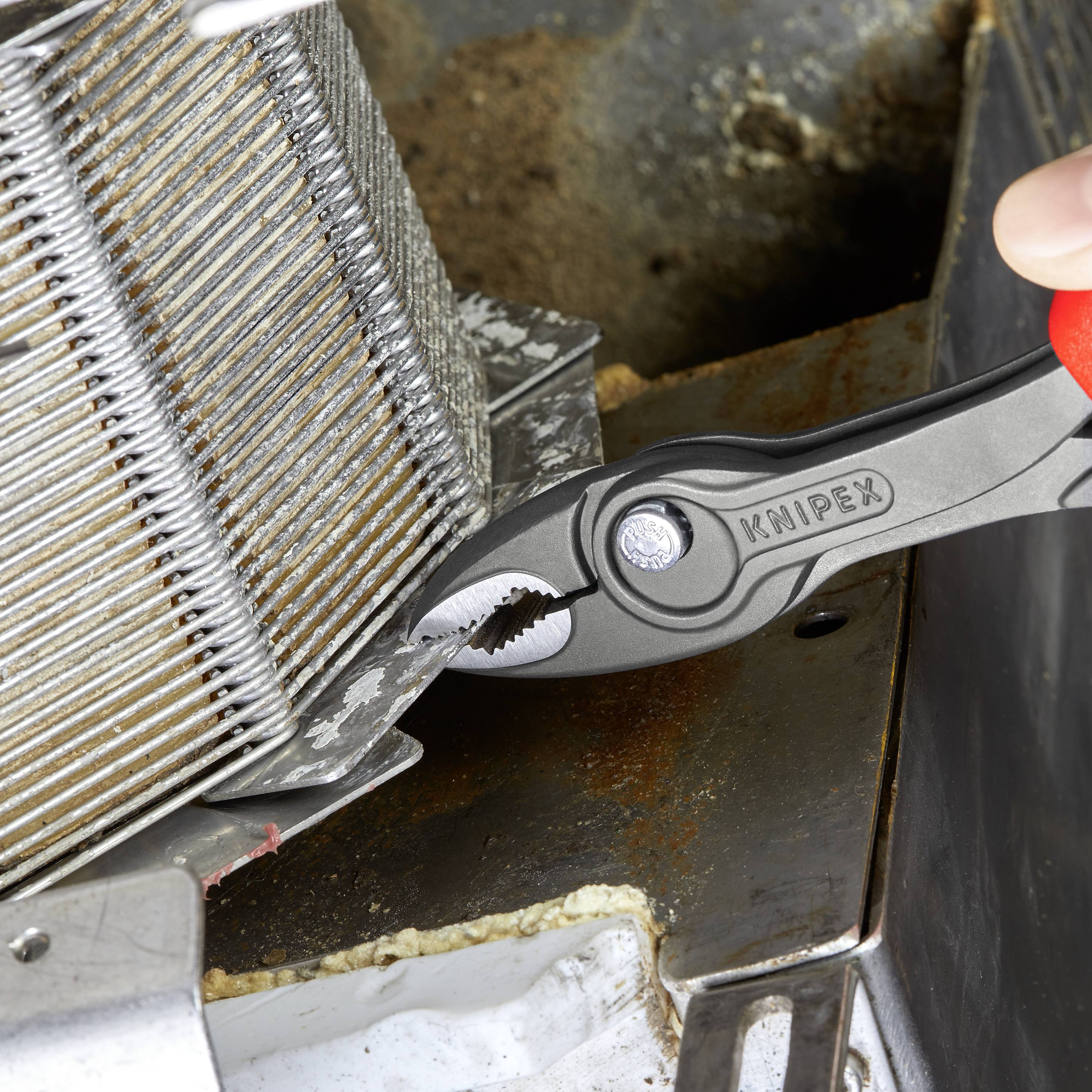 Eine Hand verwendet eine Knipex-Zange, um eine Metallverbindung zwischen zwei Kühlerlamellen festzuziehen oder zu lösen.