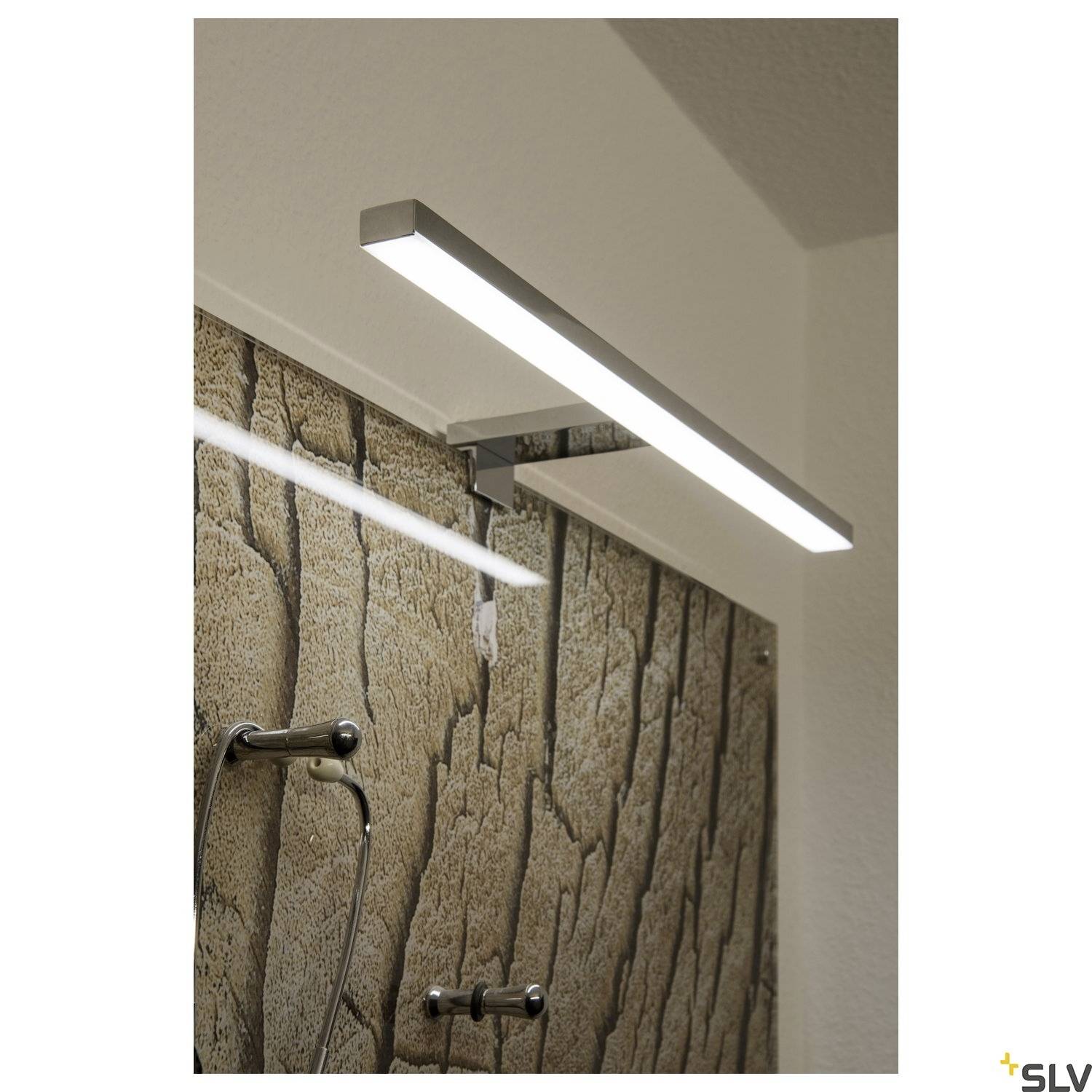 Eine rechteckige, moderne LED-Wandleuchte beleuchtet eine gemusterte Wand und einen Handtuchhalter in einem Badezimmer.