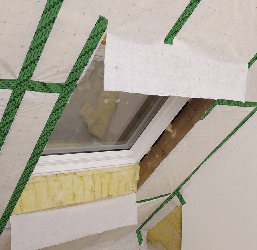 Dachboden mit Dachfenster wird isoliert. Dämmmaterial und Dampfsperrfolie mit grünem Klebeband fixiert.