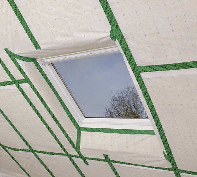 Fenster mit Blick nach draußen in einer Decke mit grünen Dichtungen und Isolierfolie eingebaut. Heller blauer Himmel sichtbar.