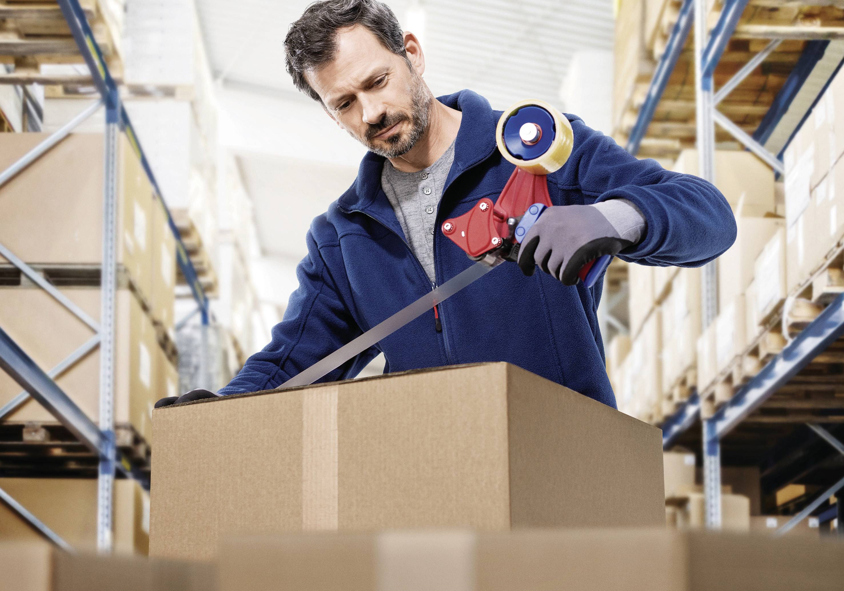 Ein Mann klebt ein Paket in einem Lager ab. Im Hintergrund sind Regale mit Kartons sichtbar.