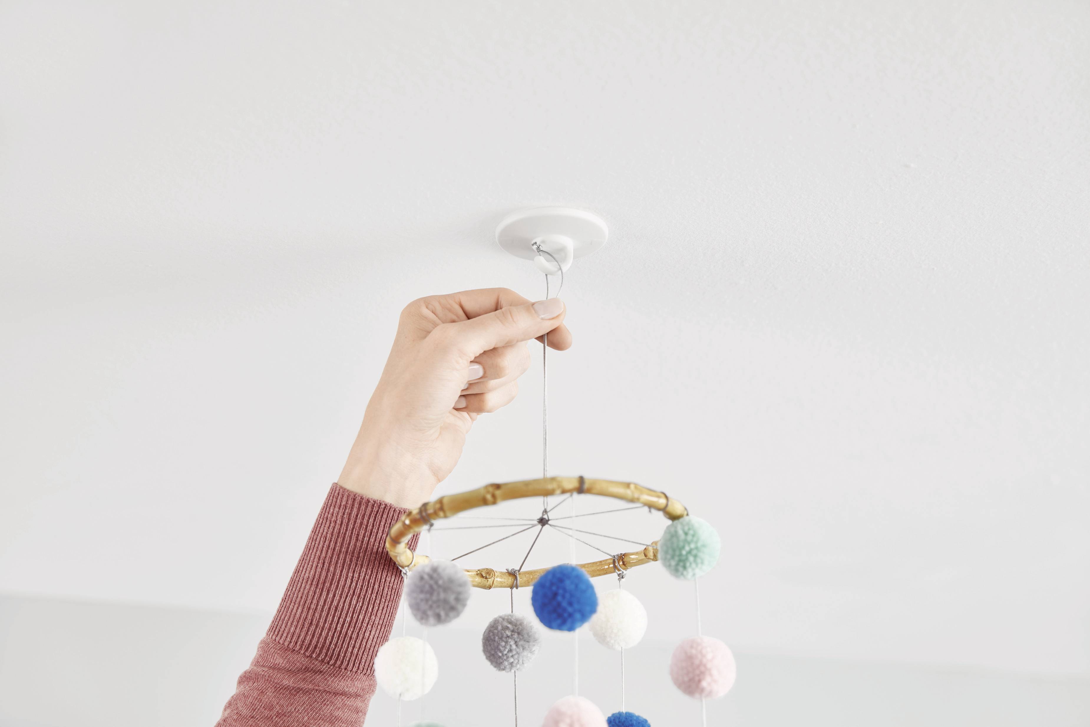 Eine Hand befestigt ein Mobile aus bunten Filzkugeln an der Decke.